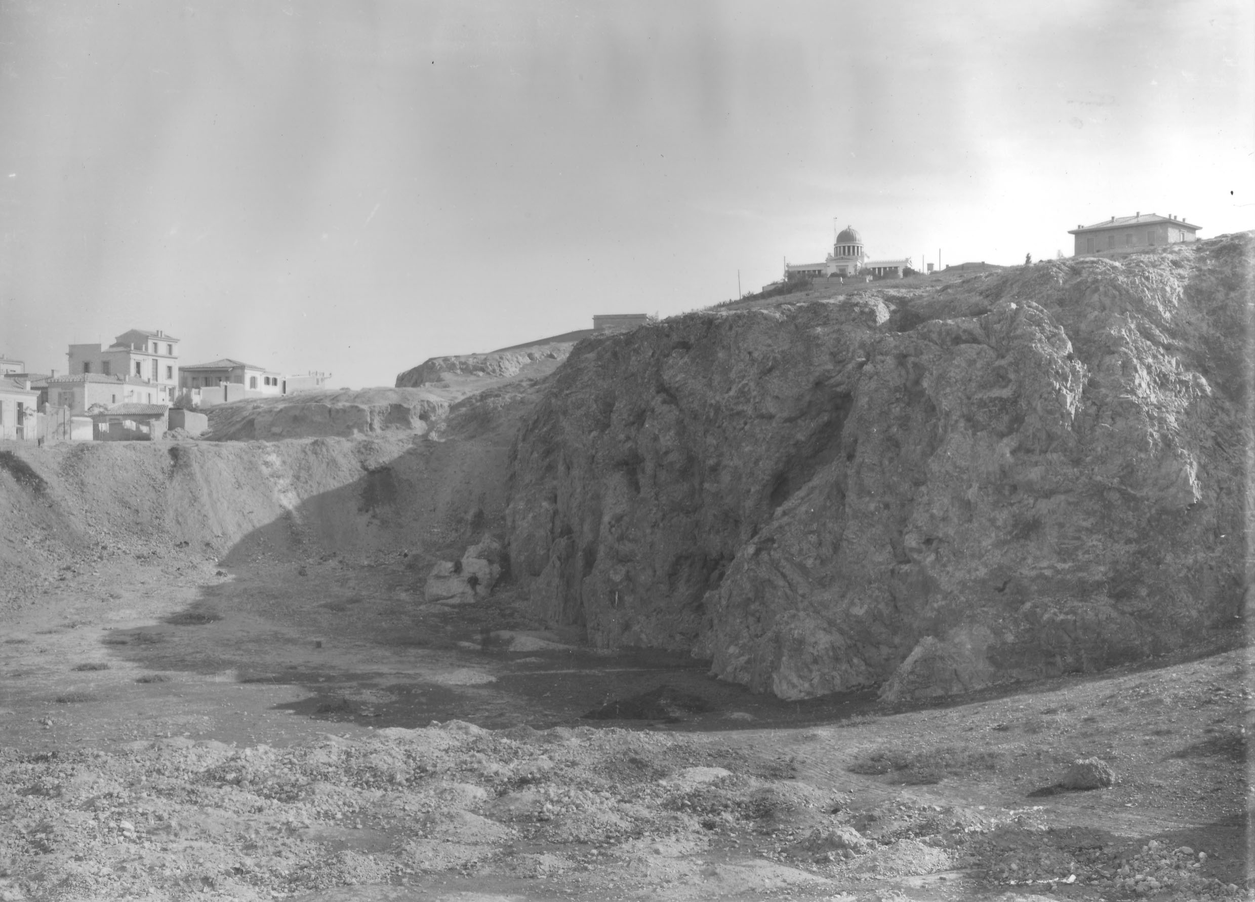 Το χάσμα του αρχαίου βαράθρου προτού επιχωματωθεί: εδώ το στέφει ο θόλος του Αστεροσκοπείου· αριστερά, η συνοικία των Πετραλώνων (Nicholson Museum, Professor W.J. Woodhouse Collection).